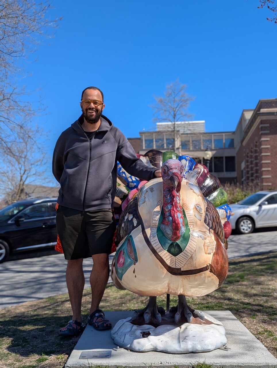John Hilliard standing next to a colorful painted turkey sculpture in a Brookline park.