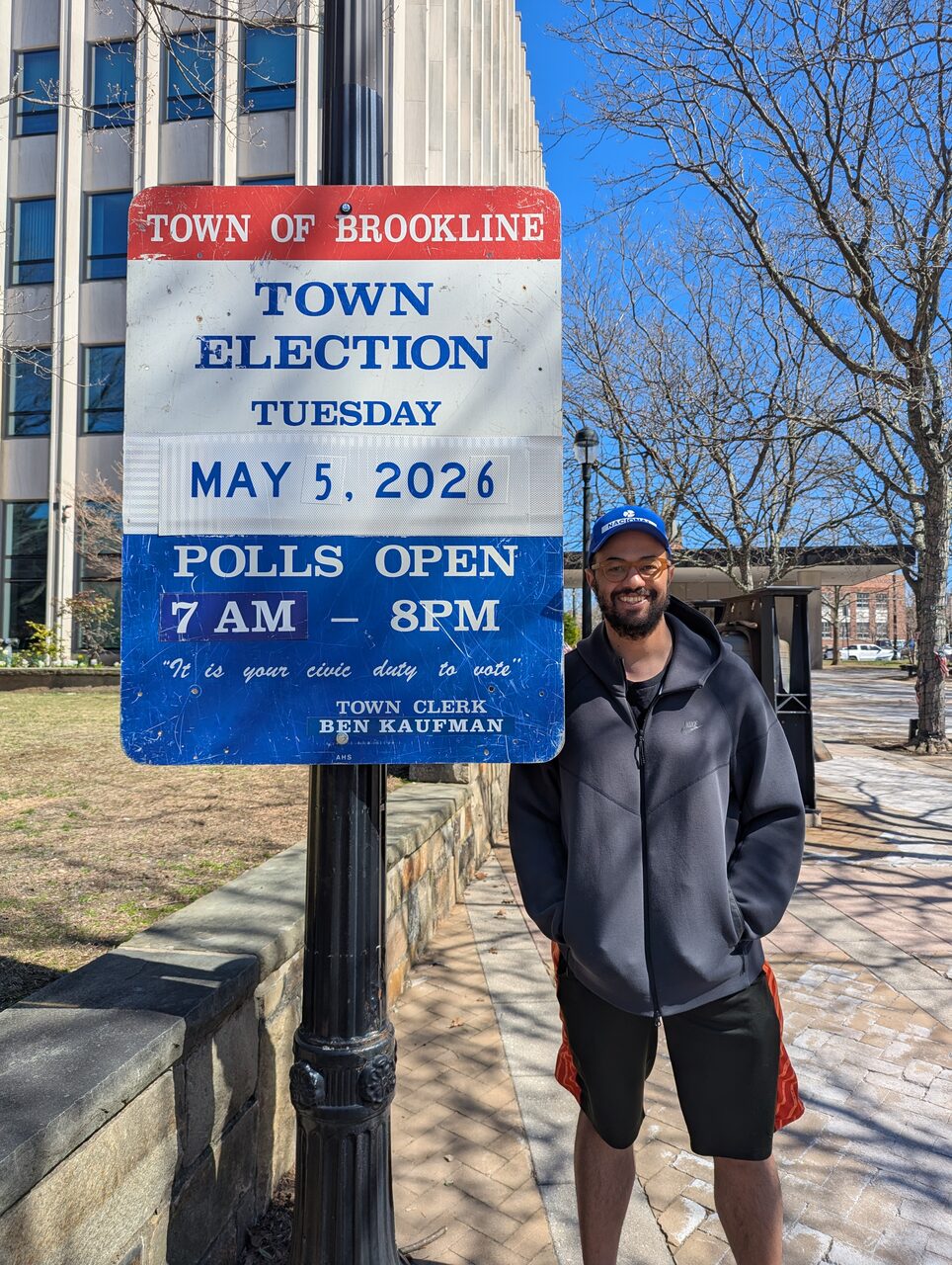 John Hilliard standing next to an official Town of Brookline sign announcing the Town Election on Tuesday, May 5, 2026, polls open 7 AM to 8 PM.