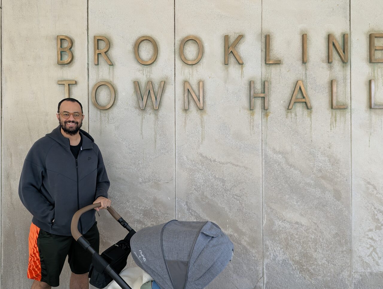John Hilliard with a stroller in front of the Brookline Town Hall sign engraved in stone.